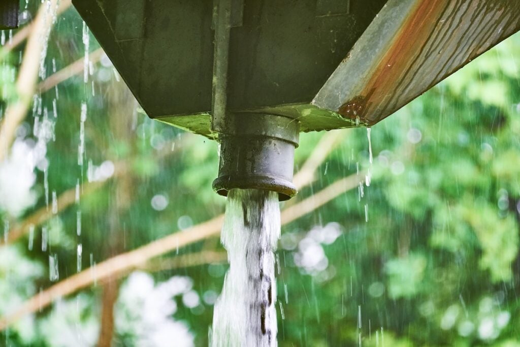 Large amount of water running from a scupper box down a chain of metal rings due to heavy rain