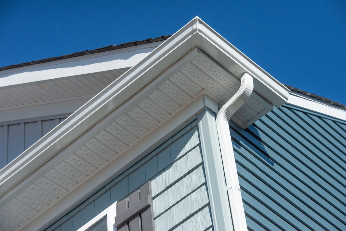 Colonial white gutter guard system, fascia, drip edge, soffit providing ventilation to the attic, with pacific blue vinyl horizontal siding at a luxury American single family home neighborhood USA